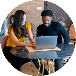 Man and woman sitting at a table with a laptop, actively discussing and collaborating with each other.